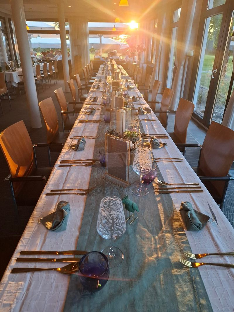 Lange gedeckte Tafel im Restaurant, durch die Fenster der Golfplatz im Abendlicht