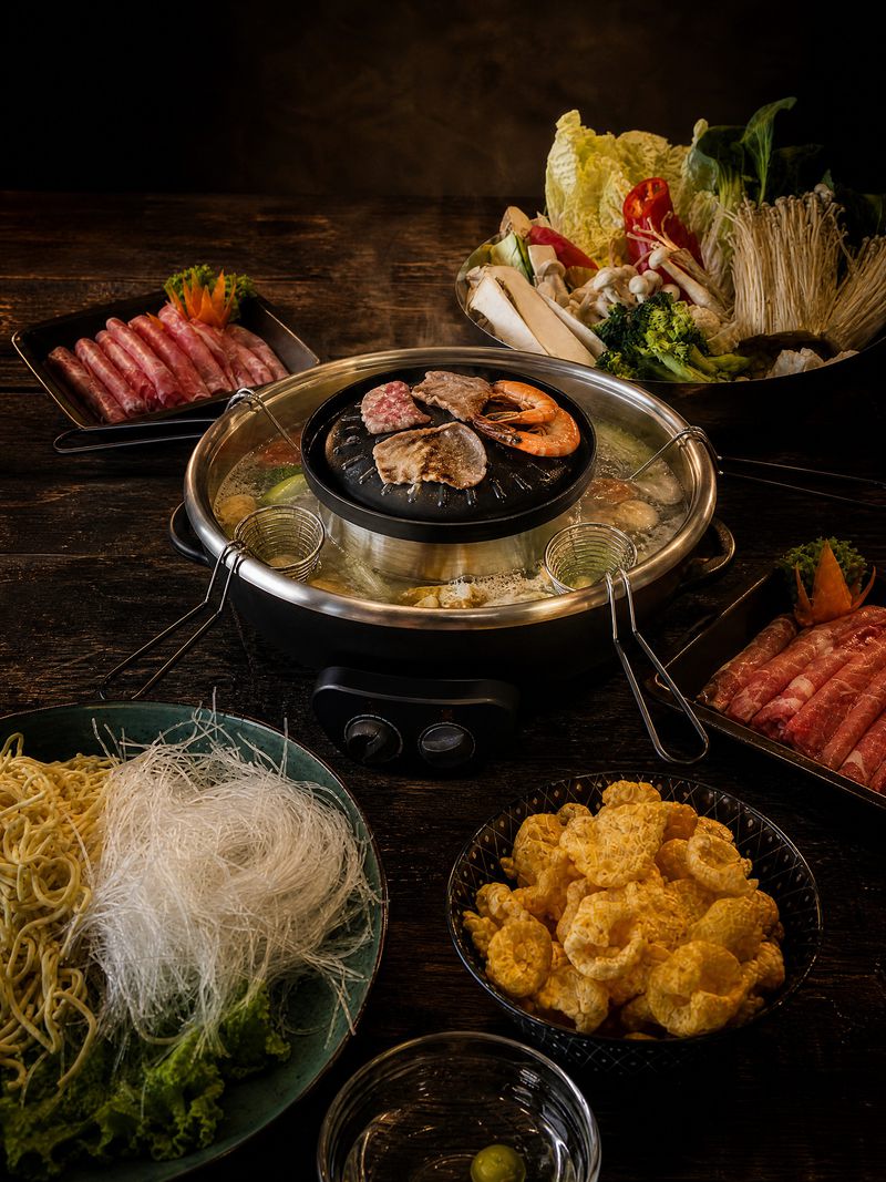 Hot Pot am Tisch: in der Mitte die Grillplatte, rundherum die Brühe, daneben Nudeln, Gemüse und Fleisch